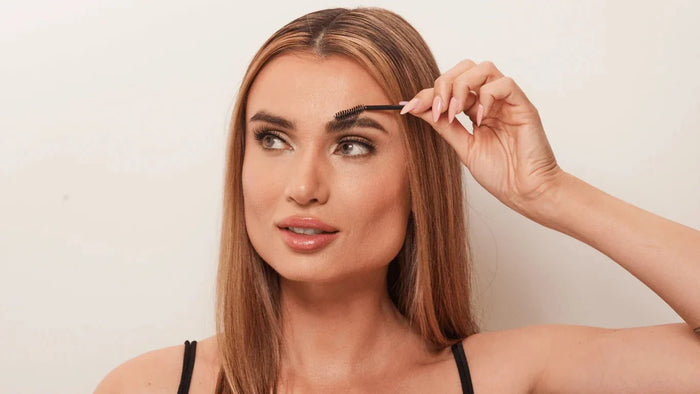 A girl brushing her brows up with a spoolie