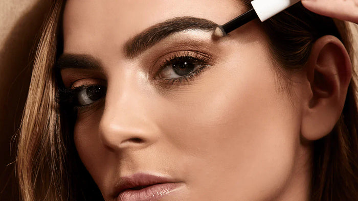 a woman applying highlighter on her brow bone