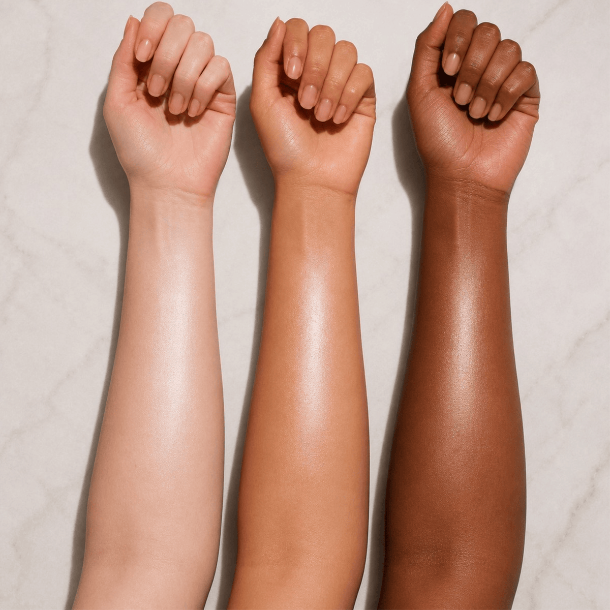Three human forearms raised against a light marble-like background, showing different skin tones from light beige to deep brown.